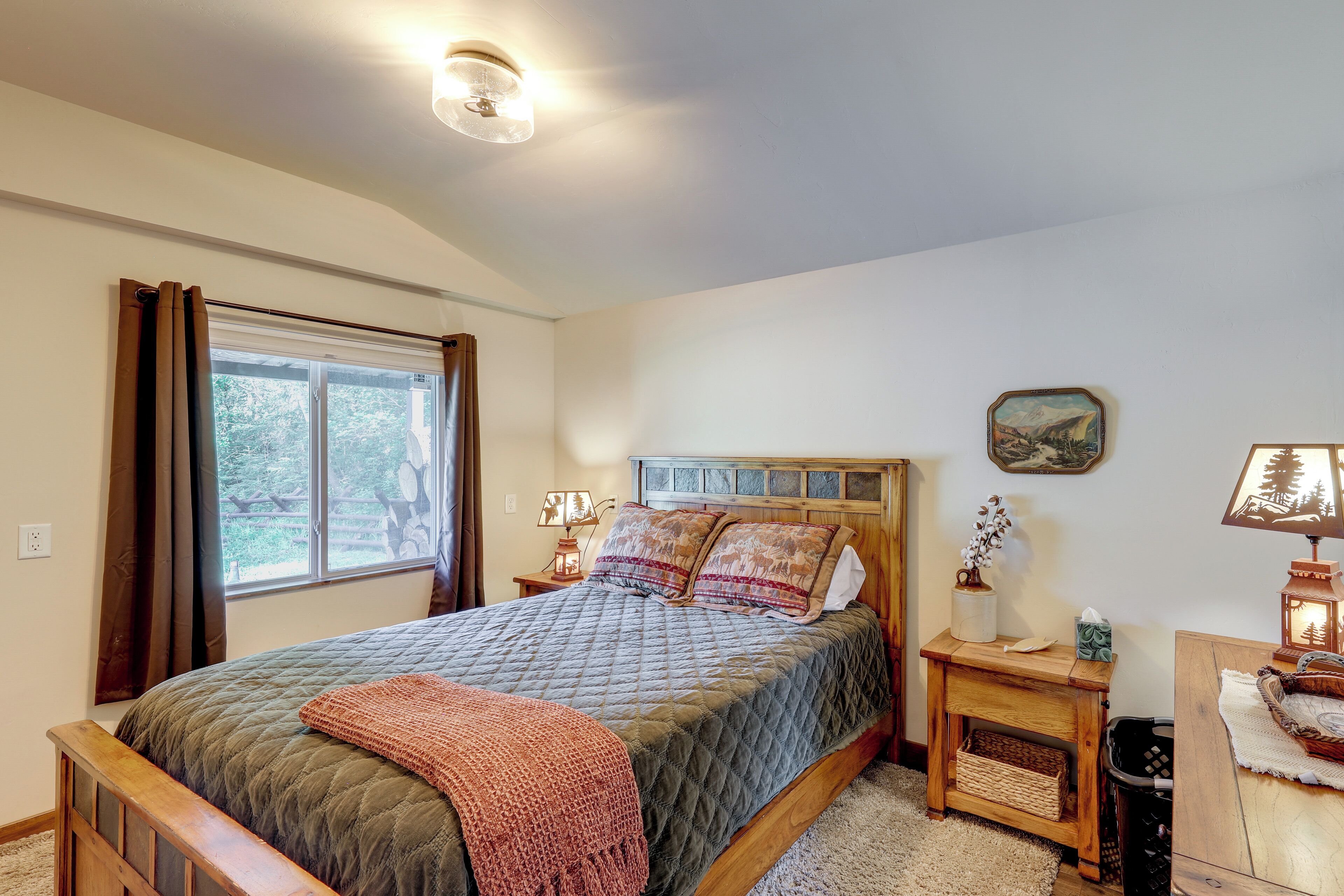 A bedroom with a bed, bedside lamps, a window with curtains, a nightstand, and a small table with a lamp.
