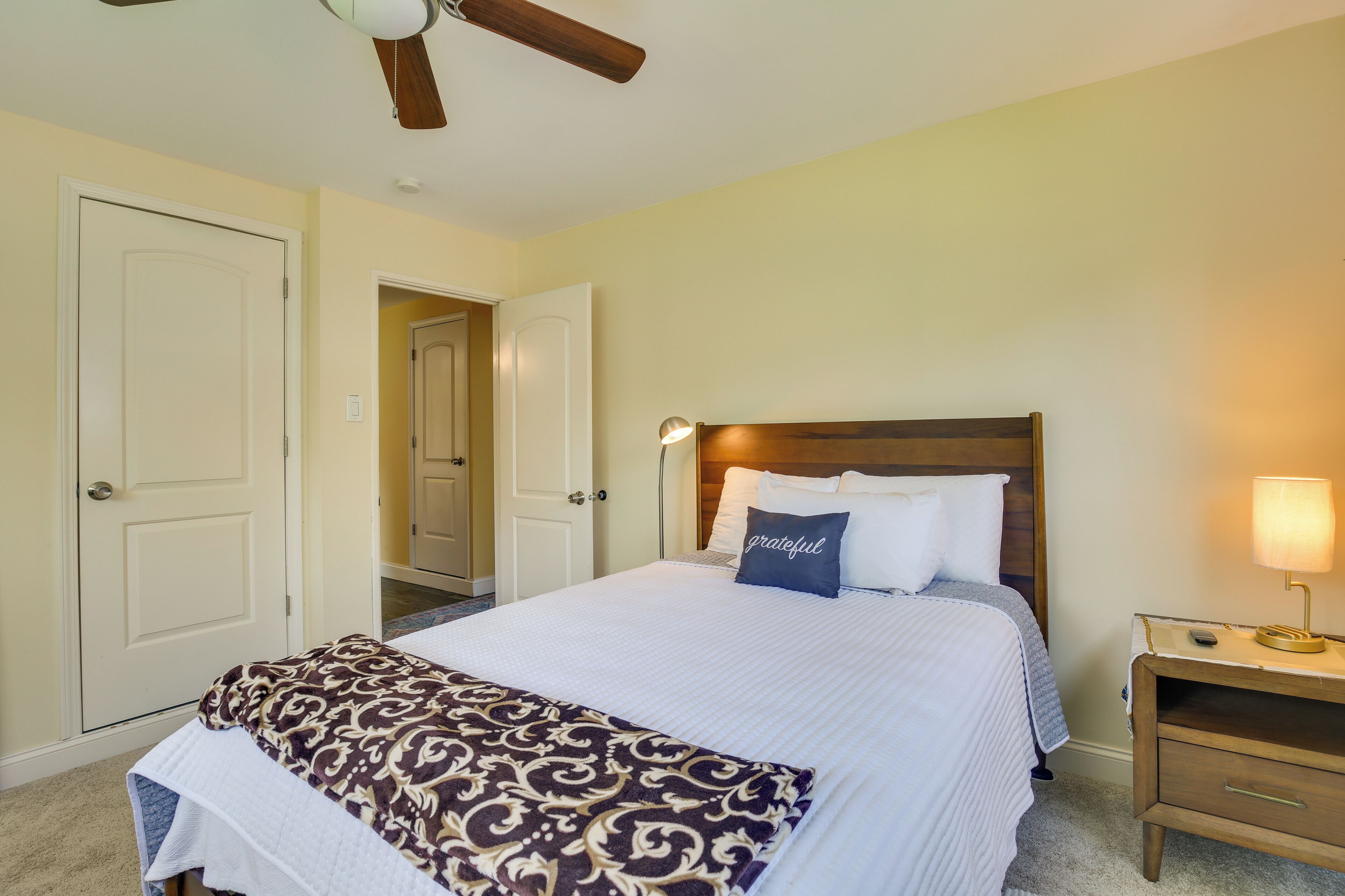 Une chambre d’hôtel avec un lit, une table de chevet, un ventilateur de plafond et une porte.