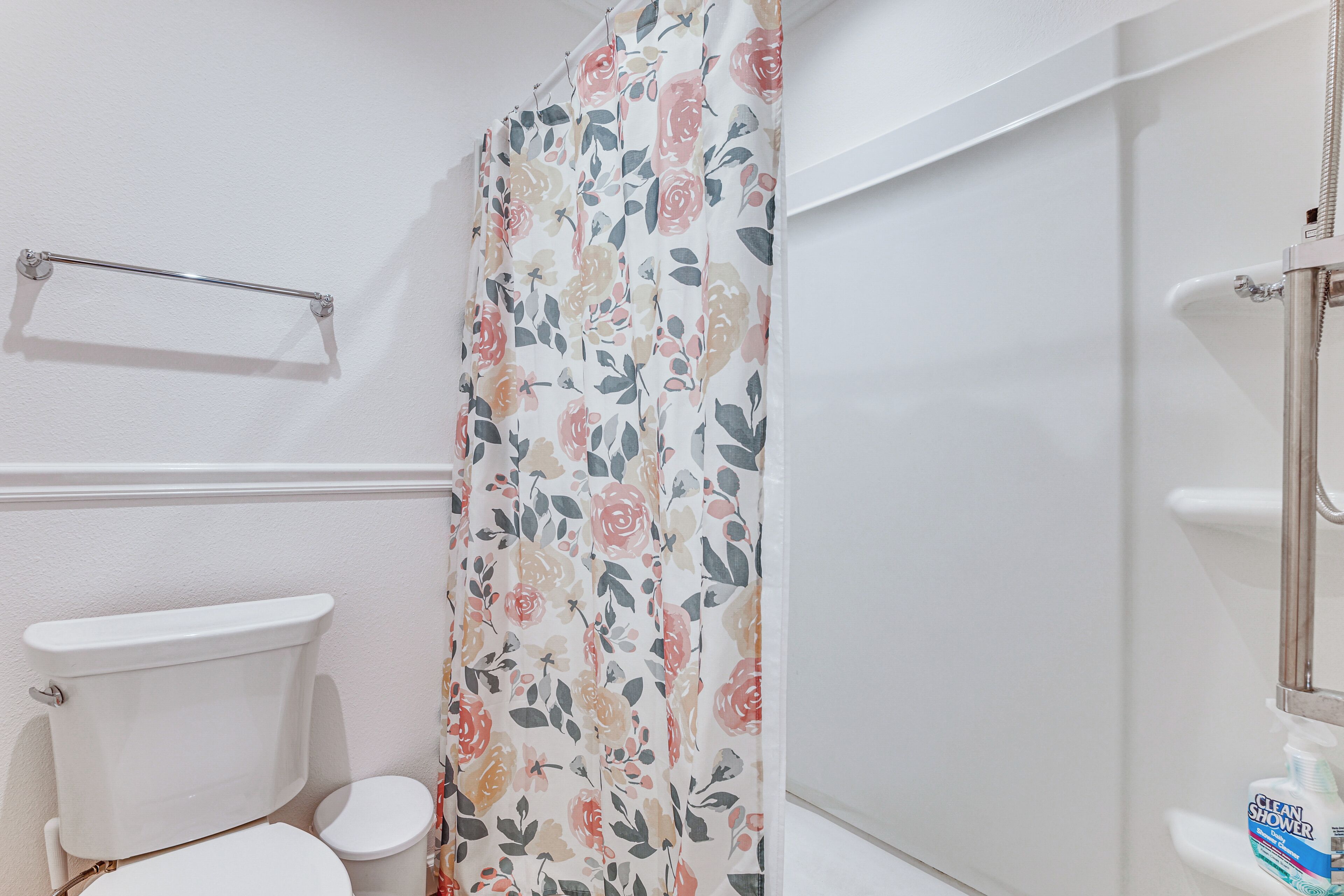 Une salle de bain avec des toilettes, un rideau de douche à motifs floraux et une barre d’appui.