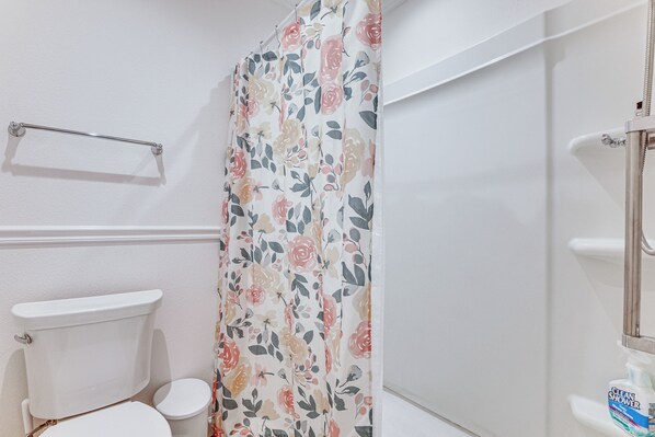 A bathroom with a toilet, a shower curtain with a floral pattern, and a handrail. - Easy Pool Access & Private Patio! Deluna Villa (Wildwood)