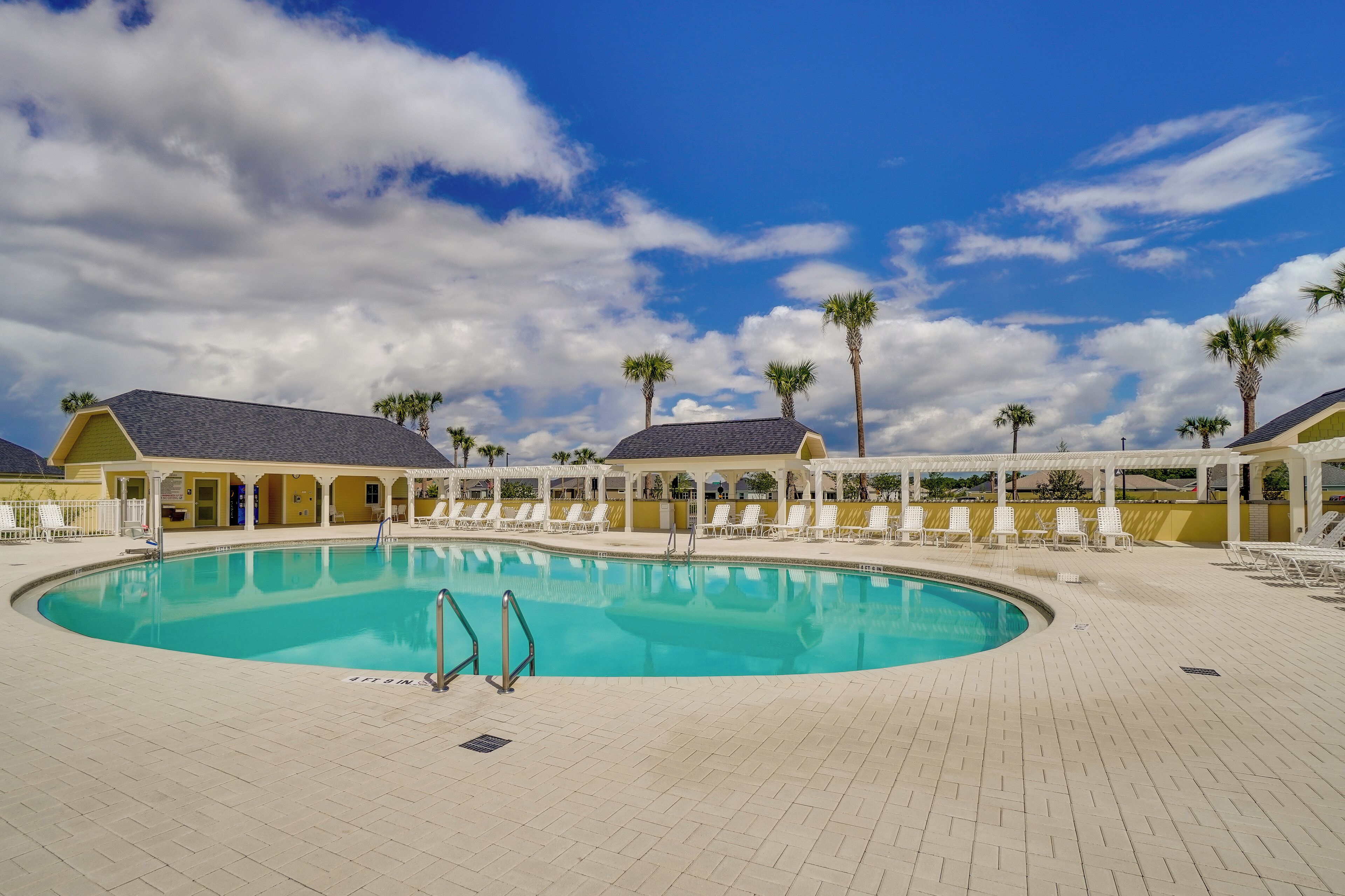 A swimming pool with lounge chairs, palm trees, and covered areas.