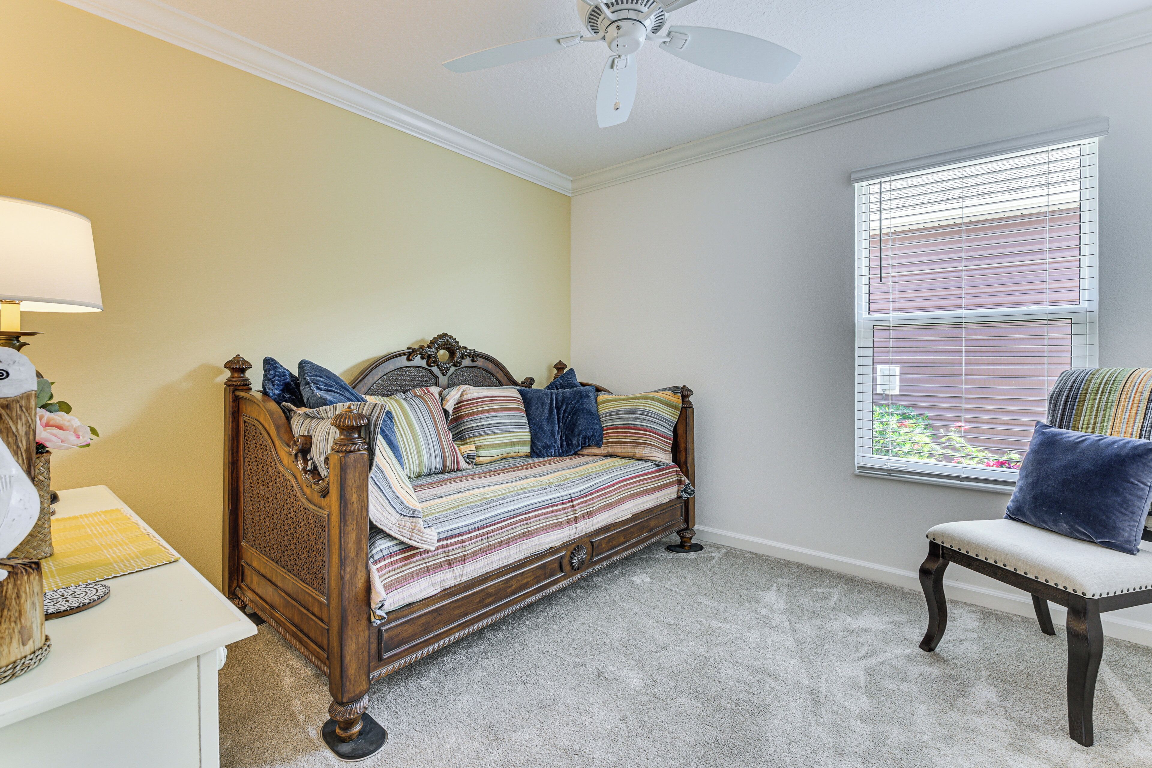A bedroom with a bed, a chair, a nightstand, a lamp, and a window with blinds.
