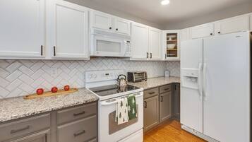 A kitchen with white cabinets, a microwave, a stove, a refrigerator, and a herringbone-patterned backsplash.