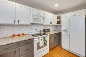 A kitchen with white cabinets, a microwave, a stove, a refrigerator, and a herringbone-patterned backsplash. - Home Near Air Force, Great Wolf, Ford Amphitheater (Colorado Springs)