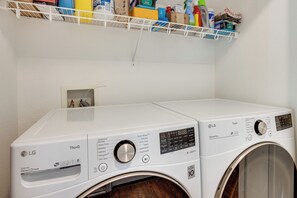 A laundry room with two white LG washing machines, a shelf above with various items, and a small window. - Home Near Air Force, Great Wolf, Ford Amphitheater (Colorado Springs)