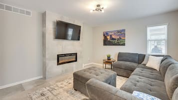 A living room with a sectional sofa, a fireplace, a mounted TV, and a painting on the wall.