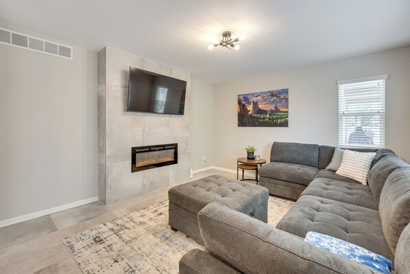 A living room with a sectional sofa, a fireplace, a mounted TV, and a painting on the wall. - Home Near Air Force, Great Wolf, Ford Amphitheater (Colorado Springs)