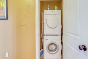 Pequeña lavandería con lavadora y secadora apiladas, un escoba y una puerta con picaporte plateado.