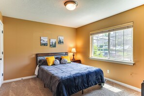 Un dormitorio con cama, mesita de noche, lámpara y ventana con vista a un barrio.