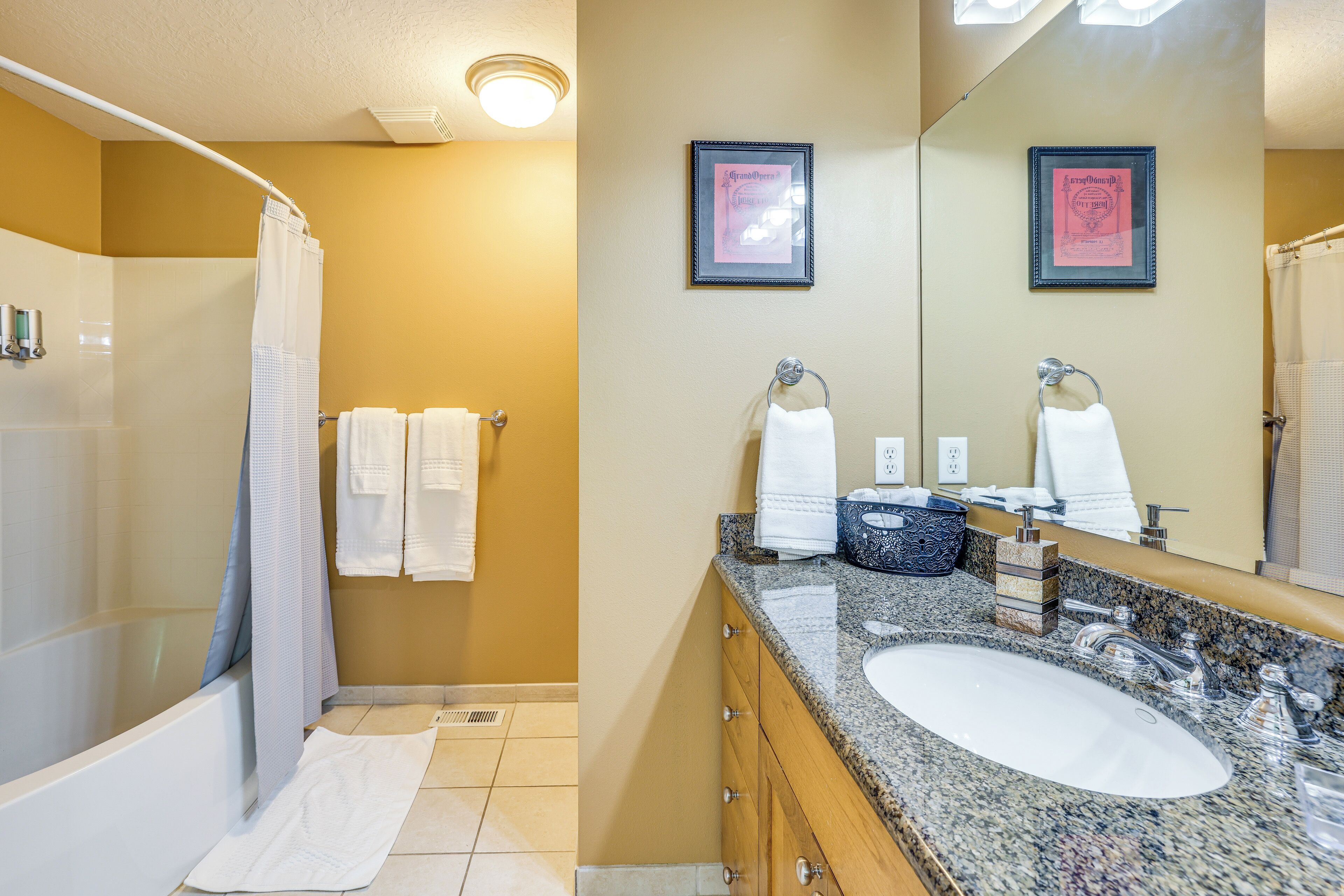 Une salle de bain avec une baignoire, un lavabo et un miroir. Des serviettes sont accrochées au mur et un tableau encadré est placé au-dessus du miroir.