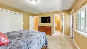 A bedroom with a bed, dresser, TV, and a door leading to another room.