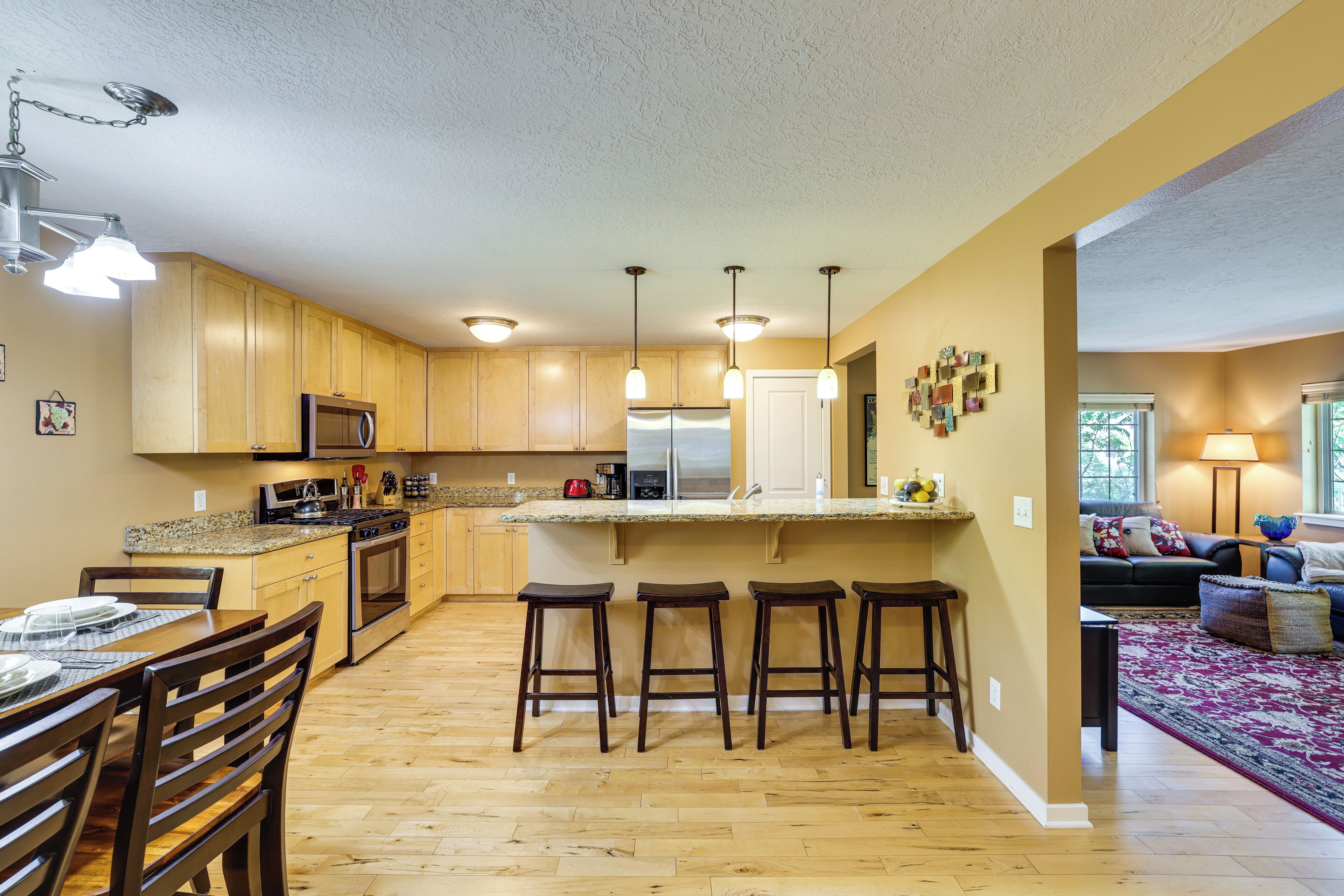 A kitchen with wooden cabinets, a central island with stools, a microwave, and a refrigerator.