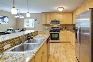 Cocina con encimeras de granito, electrodomésticos de acero inoxidable, armarios de madera y una ventana que proporciona luz natural.