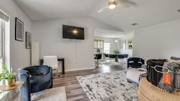 A modern living room with a flat-screen TV, a ceiling fan, a dining area with a table and chairs, and a large mirror.