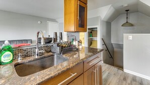 Eine Küche mit Granit Arbeitsplatten, Holzschränken, einer Edelstahl-Spüle und einer Pendelleuchte.