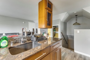 A kitchen with granite countertops, wooden cabinets, a stainless steel sink, and a hanging light fixture.