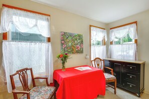 A dining area with a red tablecloth, two chairs, a vase with flowers, a cabinet, and a painting on the wall. - Cozy Vintage in Friendly Neighborhood, 2 Mi to UO! (Eugene)