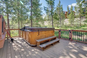 Eine Holzterrasse mit Whirlpool, Holzbanken und Blick auf einen bewaldeten Bereich.