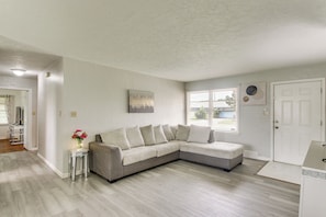 En moderne stue med en hjørnesofa, et lille sofabord med en vase, en dør og et vindue.