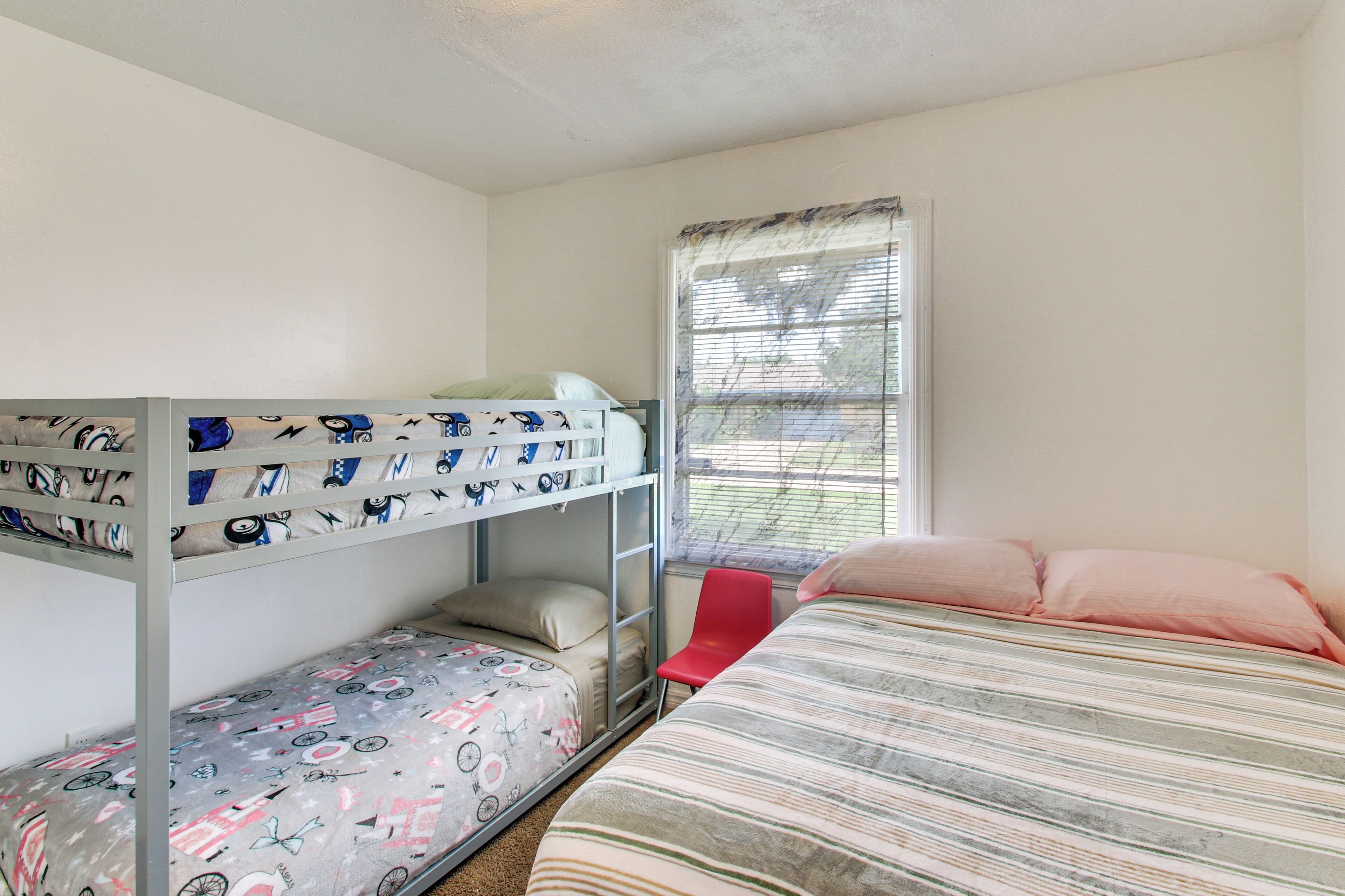 Une chambre avec des lits superposés, un lit simple, une fenêtre avec des stores et une chaise rouge.