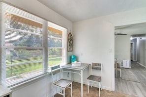 Une piĂšce comprenant une table Ă manger, deux chaises, une petite table avec un bol, et une fenĂȘtre avec des stores.
