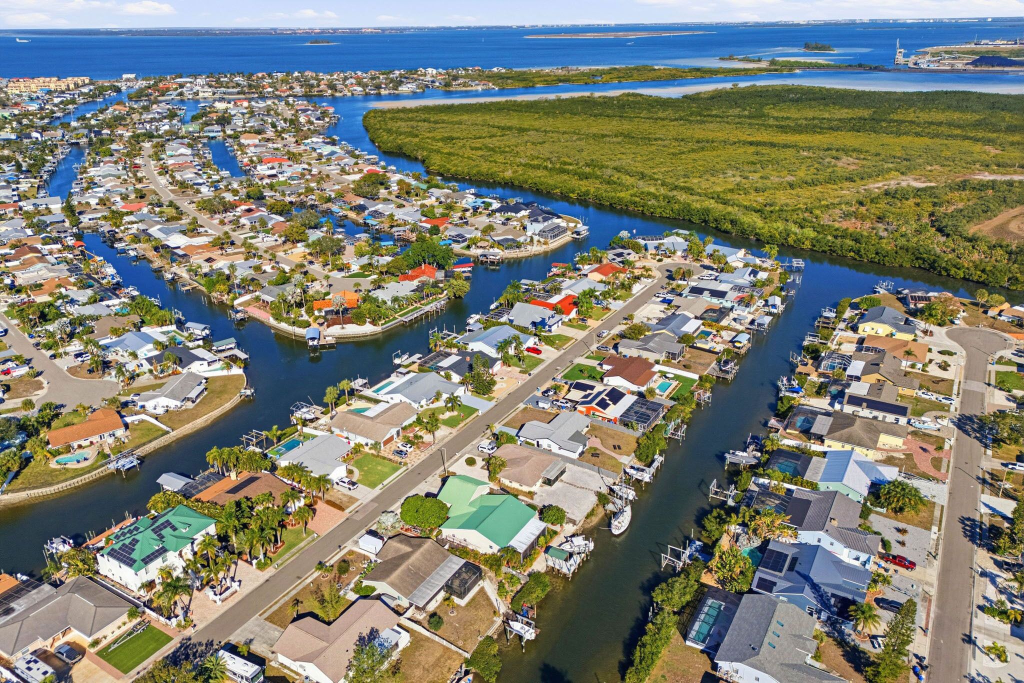 An aerial view of a coastal residential area with houses, a marina, and a river.