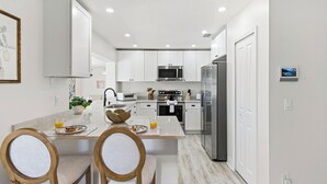 Une cuisine moderne avec des meubles blancs, des appareils en acier inoxydable et un coin repas comprenant des chaises et une table.