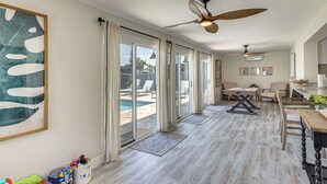 Une pièce spacieuse dotée d’une grande porte-fenêtre coulissante donnant sur une piscine, de ventilateurs de plafond et d’un coin repas avec une table et des chaises.
