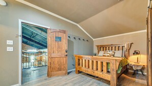 A room with a wooden bed, a small table with a lamp, and a door leading to a balcony. - Steps to Lake Granbury: Romantic 'longhorn Suite' (Granbury)