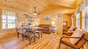 A wooden interior with a dining table, sofa, and armchair, wooden floors, ceiling fan, and framed pictures on the walls. - Idyllic Farm Setting! Granbury 'white Daisy Cabin' (Granbury)
