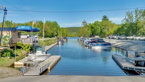 A marina with boats docked, a dock with a covered area, and a building with a blue awning. - Boat, Fish & Hike! All-season Schroon Lake Getaway (Schroon Lake)