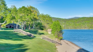 A lakeside property with a grassy area, a wooden bridge, and a small building near the water. - Boat, Fish & Hike! All-season Schroon Lake Getaway (Schroon Lake)