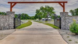 A gated entrance with a stone wall, a wooden pergola, and a pathway leading to a building. - Tranquil 'red Magnolia Cabin' Near Lake Granbury! (Granbury)