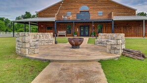 A wooden barn-style building with a covered porch, stone pillars, and a large decorative planter. - Tranquil 'red Magnolia Cabin' Near Lake Granbury! (Granbury)