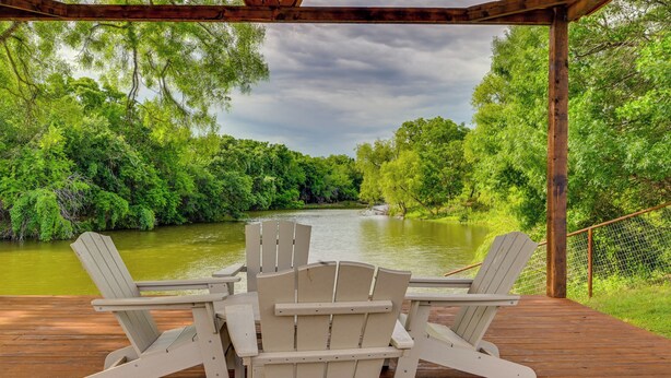 A wooden deck with two Adirondack chairs facing a river surrounded by greenery. - Tranquil 'red Magnolia Cabin' Near Lake Granbury! (Granbury)