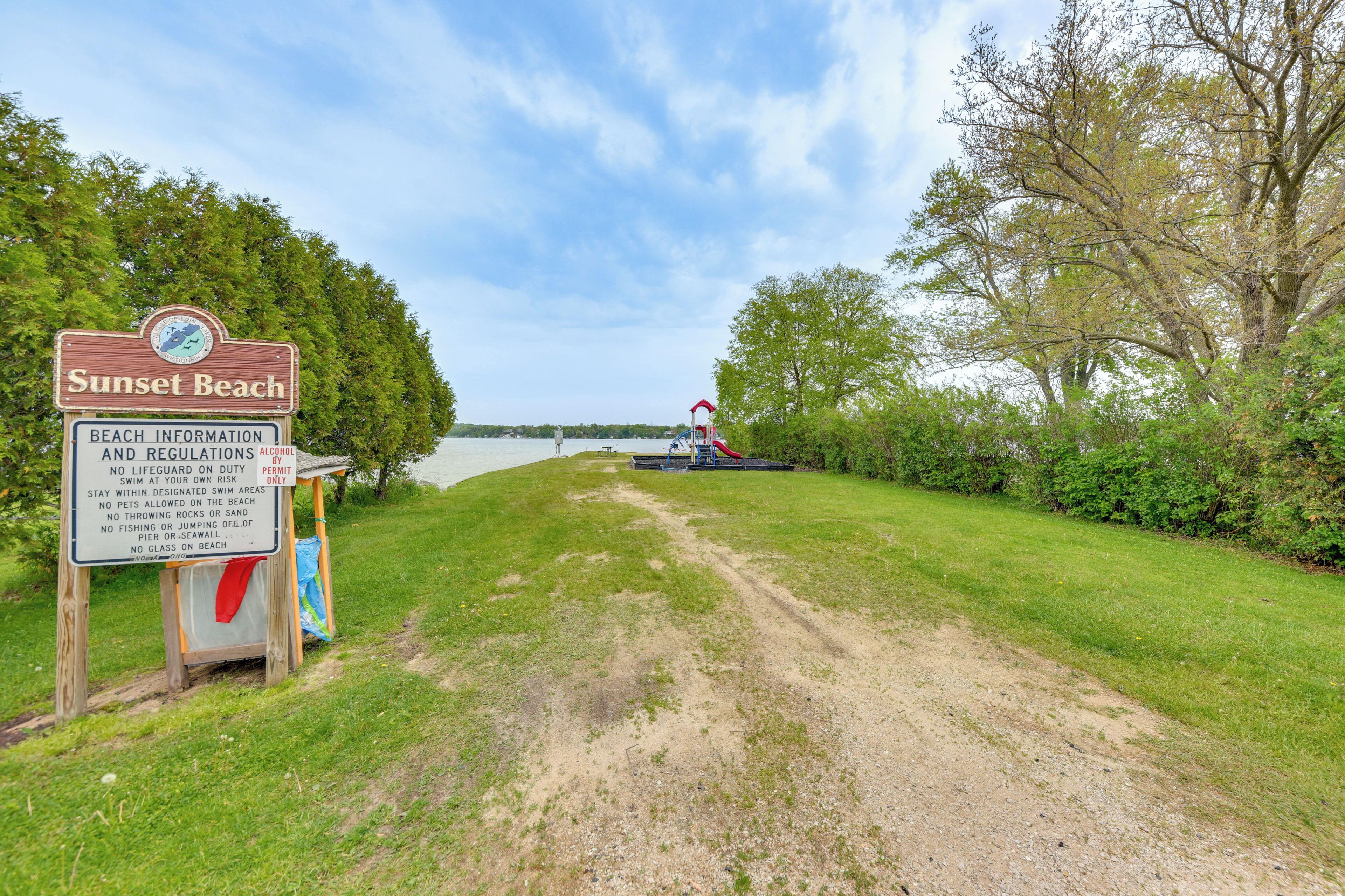 A beach sign with regulations and a path leading to a beach area.