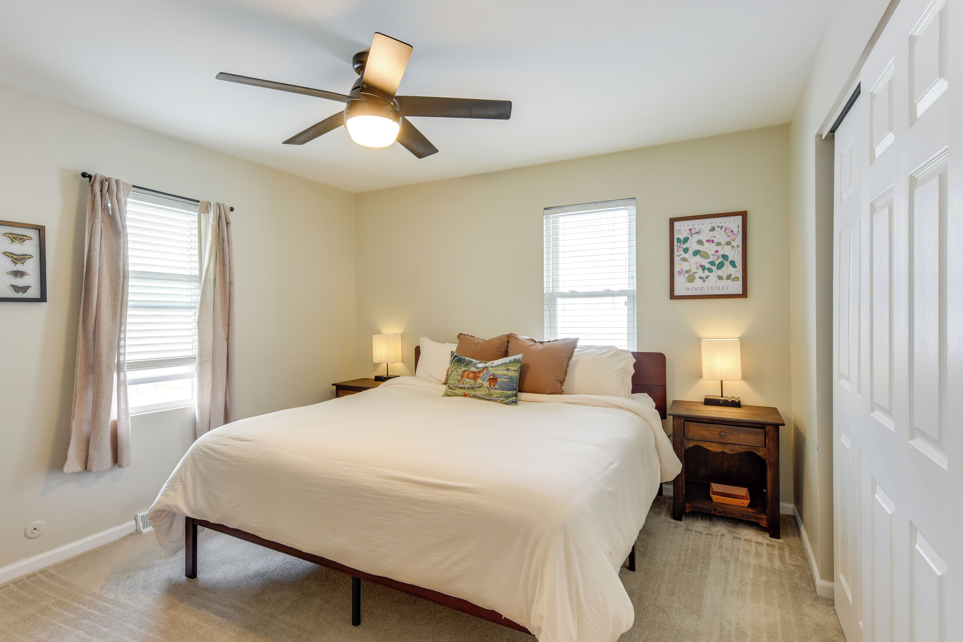 A bedroom with a bed, ceiling fan, bedside lamps, and a window with blinds.