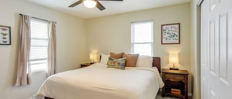 A bedroom with a bed, ceiling fan, bedside lamps, and a window with blinds.