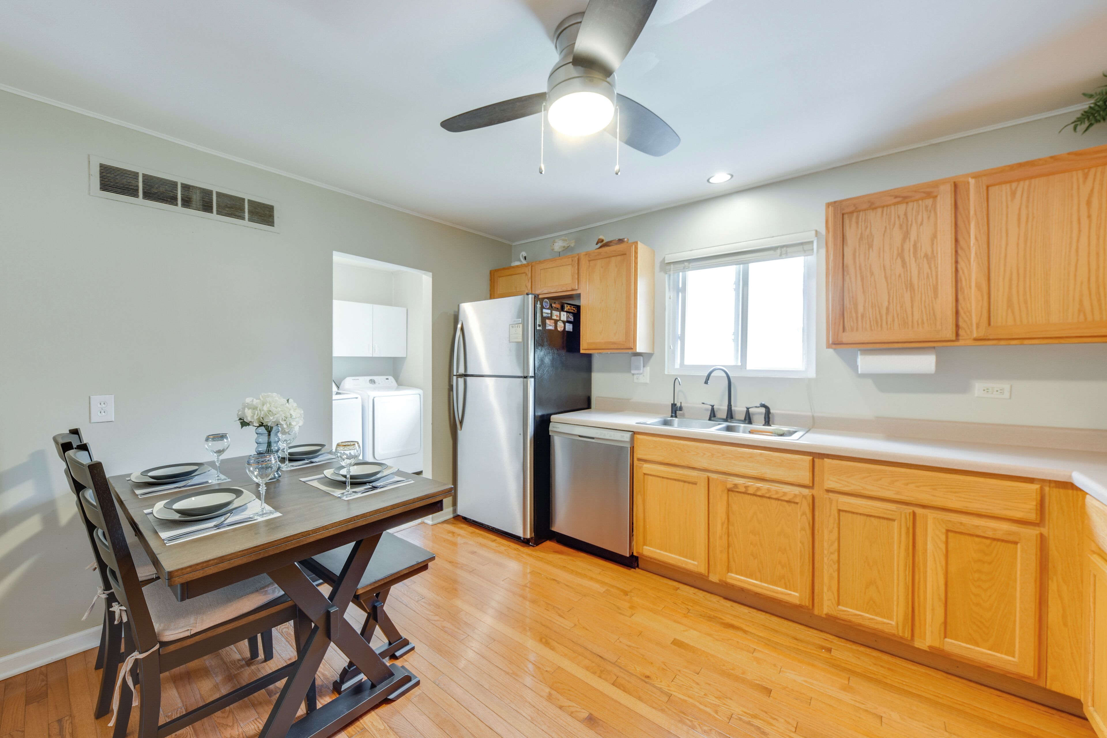 A modern kitchen with wooden cabinets, a stainless steel refrigerator, a dishwasher, and a dining table set for four.