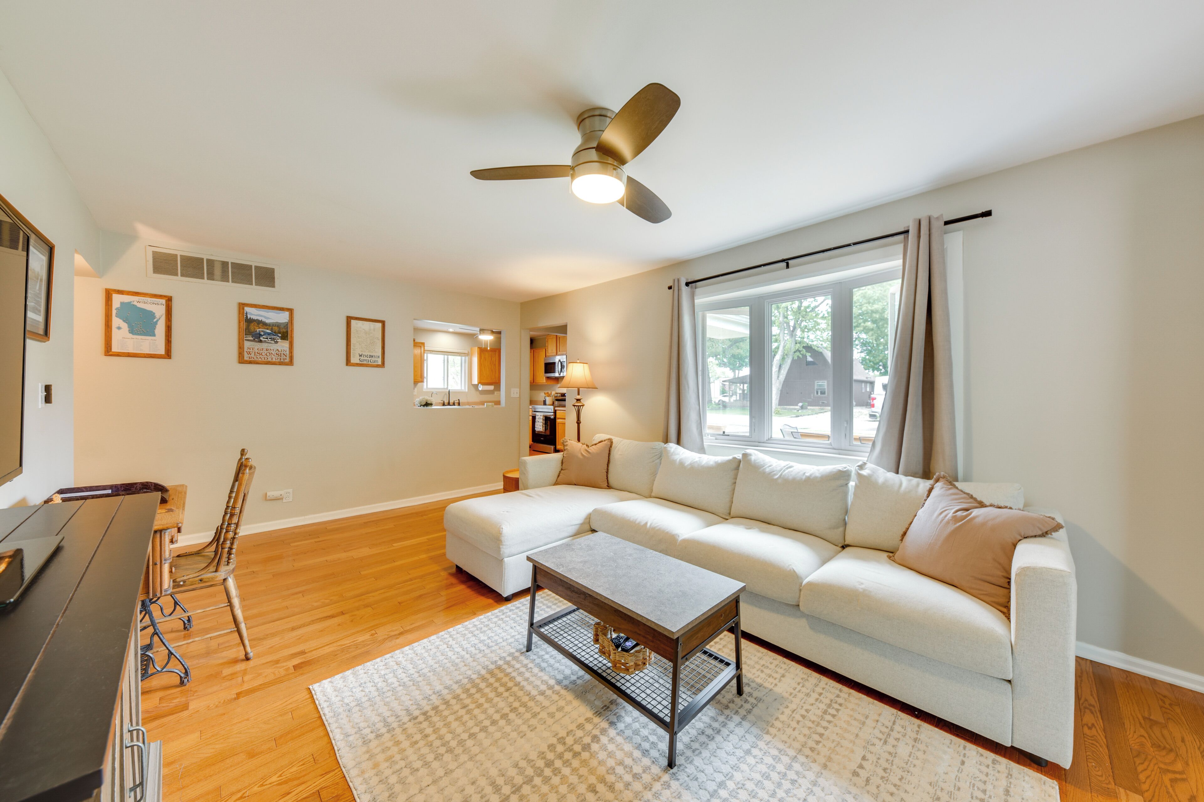 A living room with a sofa, a coffee table, a dining table with chairs, a ceiling fan, and a large window.