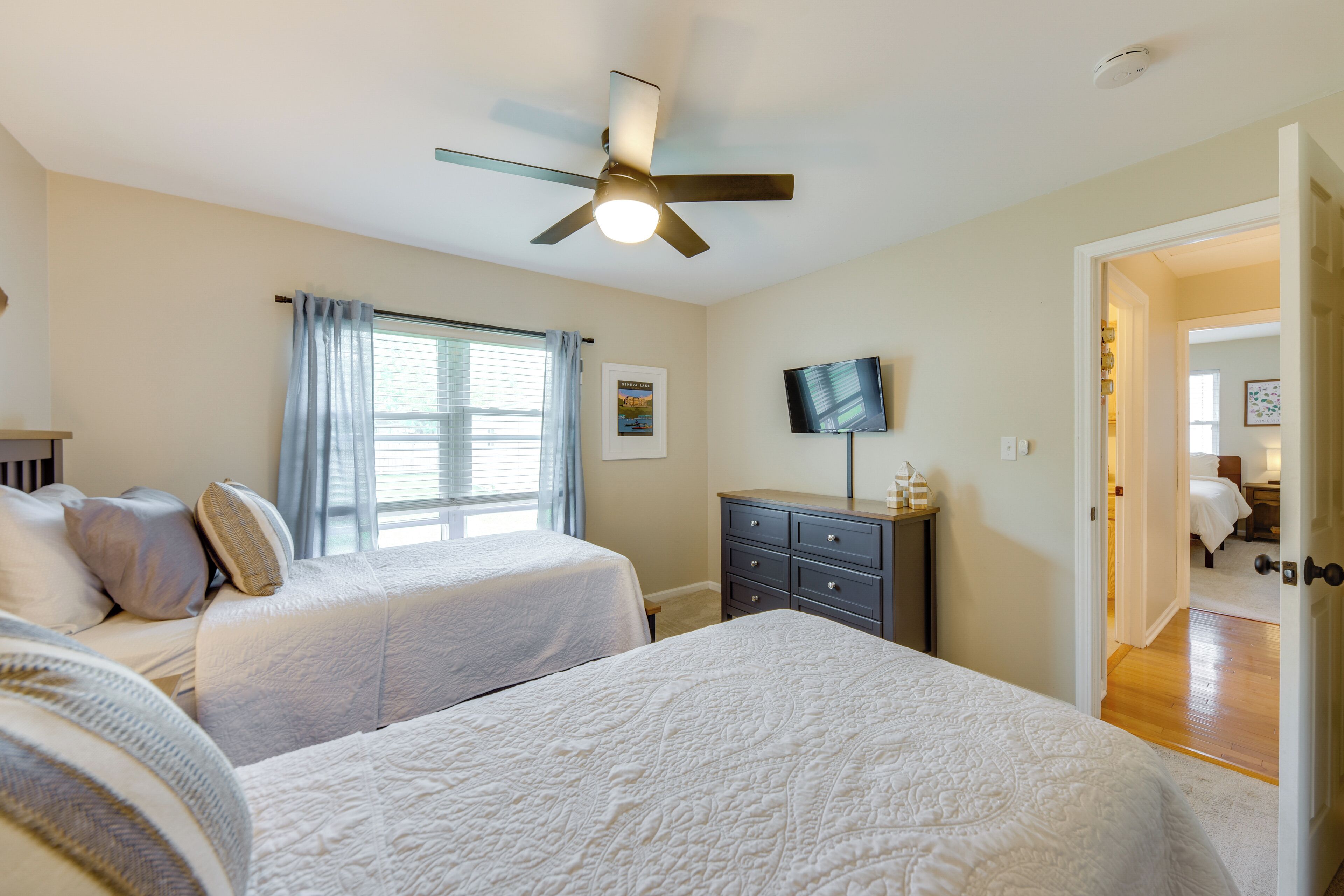 A bedroom with two beds, a ceiling fan, a TV, and a window with curtains.
