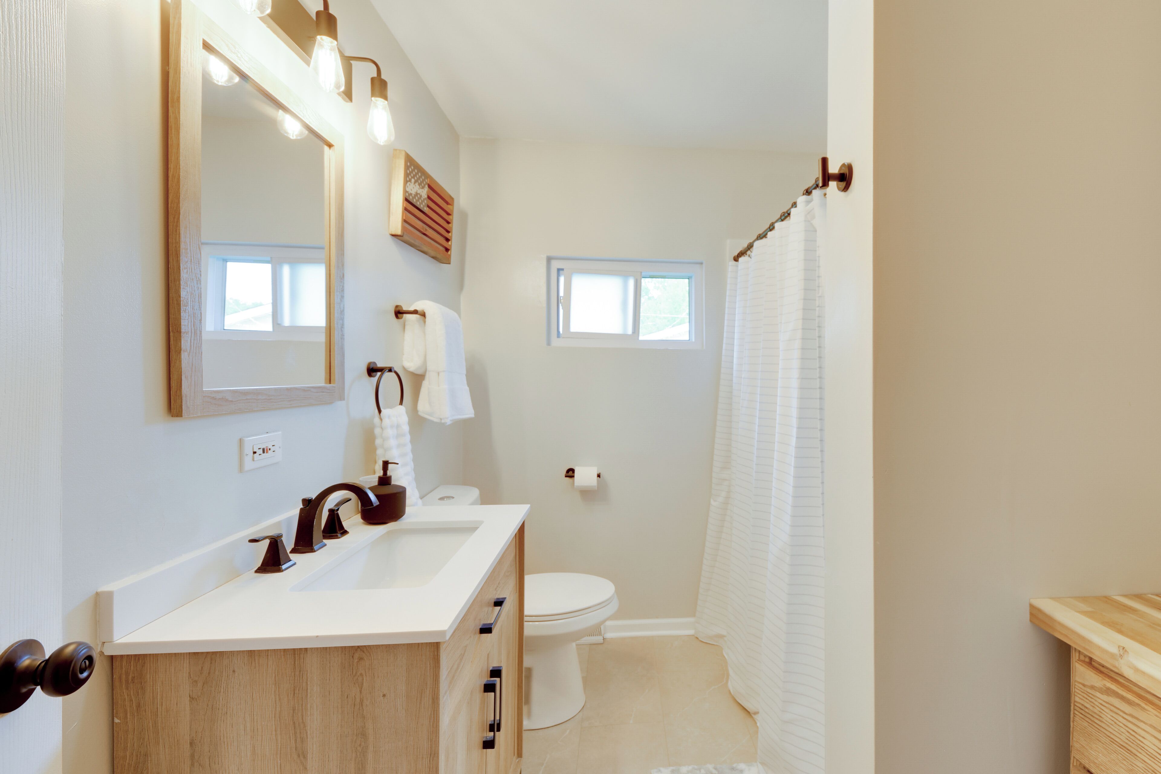 A bathroom with a wooden vanity, a mirror, a toilet, and a shower curtain.