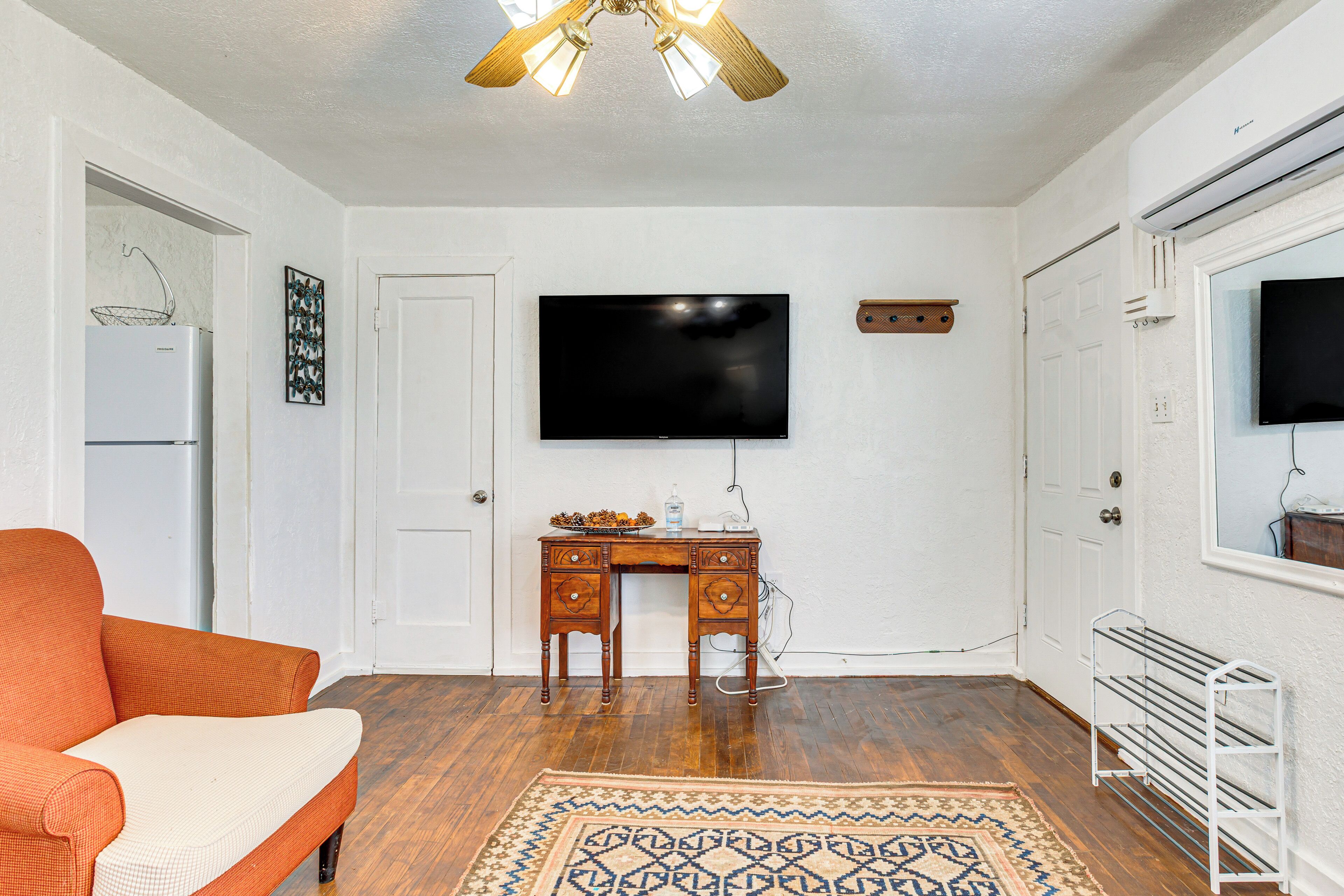 A room with a wooden desk, a television, a ceiling fan, and a patterned rug.