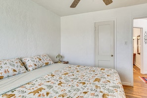 Un dormitorio con cama, almohadas, una mesita de noche, una puerta y un pasillo.