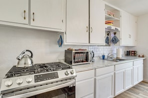 Una cocina con armarios blancos, estufa a gas, horno, microondas y pileta.