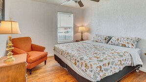 Ein Schlafzimmer mit Bett, Stuhl, Schreibtisch, Deckenventilator und einem Fenster mit Jalousien.