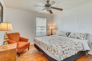 Une chambre à coucher comprenant un lit, une chaise, un bureau, un ventilateur de plafond et une fenêtre avec des stores.
