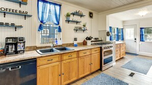 A kitchen with wooden cabinets, a coffee bar, a sink, a stove, and blue curtains. - Walk to Stetson and Historic Downtown Deland! (DeLand)