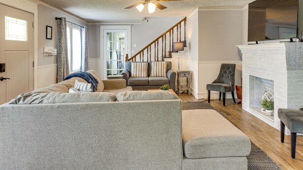 A living room with a sectional sofa, a fireplace, a ceiling fan, and a staircase leading to another room. - Walk to Stetson and Historic Downtown Deland! (DeLand)