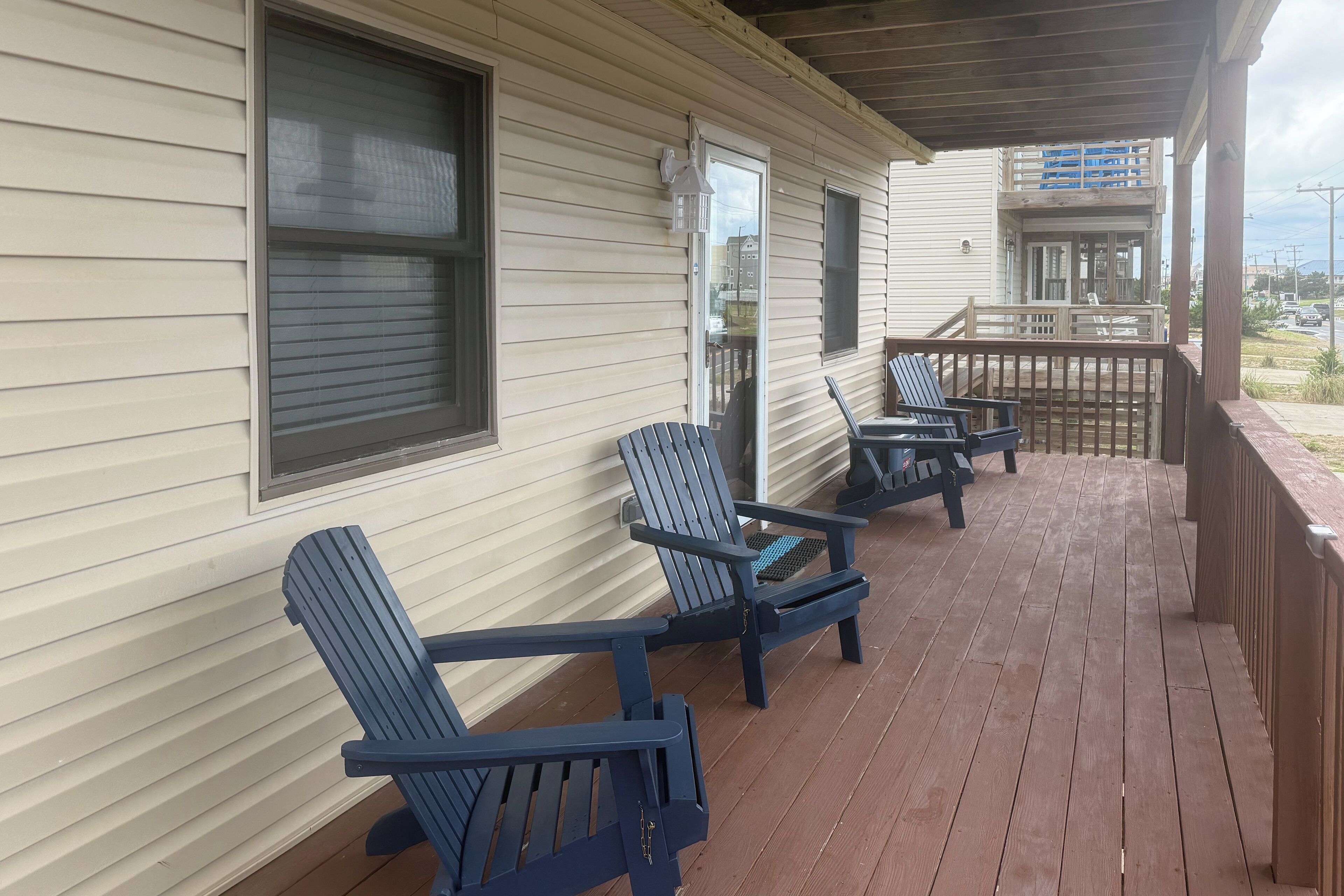 Une véranda couverte avec une terrasse en bois, deux fauteuils Adirondack et une vue sur un quartier résidentiel.